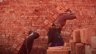 Scena del documentario “Bhaktapur – a human story”: due lavoratori trasportano mattoni su una spalla davanti a un muro rosso, presentato al Riviera International Film Festival.