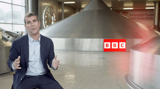 Spot “Storyworks: Campus Peroni” per BBC: uomo in giacca blu parla all’interno di un birrificio con impianti di produzione sullo sfondo.