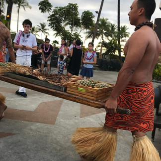 Traditional Hawaiian luau with roasted pig and performers serving food outdoors in Hawaii