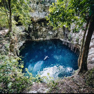 Cenote in Tulum Mexico with clear blue water surrounded by rocks and greenery