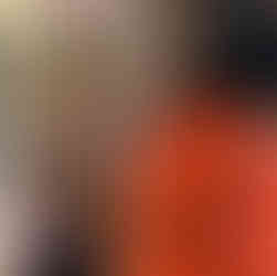 Close-up emotional reaction from surprise 60th birthday party as woman in orange dress smiles with tears in her eyes inside decorated home.