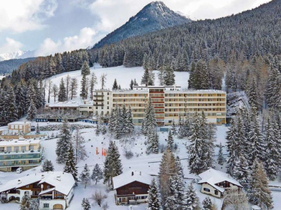Schweizer Berghotel in verschneiter Alpenlandschaft mit Tannenwald und Winterkulisse.