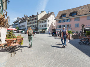Fussgängerzone in der Altstadt von Bülach mit Cafés, historischen Gebäuden und Menschen bei sonnigem Wetter