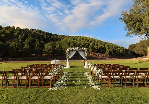 Rustic outdoor wedding ceremony at Sunmist Estate with dark wood chairs, a white floral arch