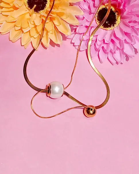 Gold necklace with a pearl on a pink background with flowers