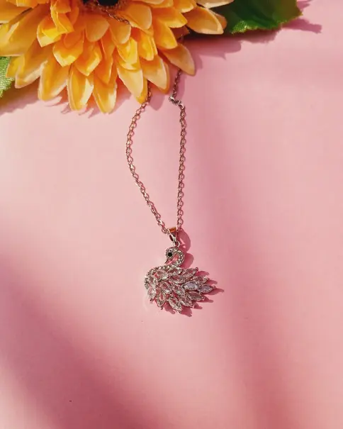 Silver necklace with a clear swan pendant hanging against a pink and yellow background
