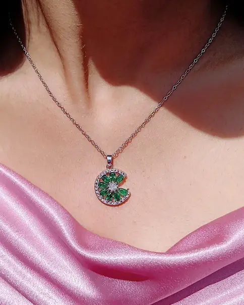 Person wearing a silver necklace with a green tourmaline pendant.