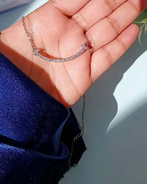 Hand holding a silver necklace with a curved bar pendant