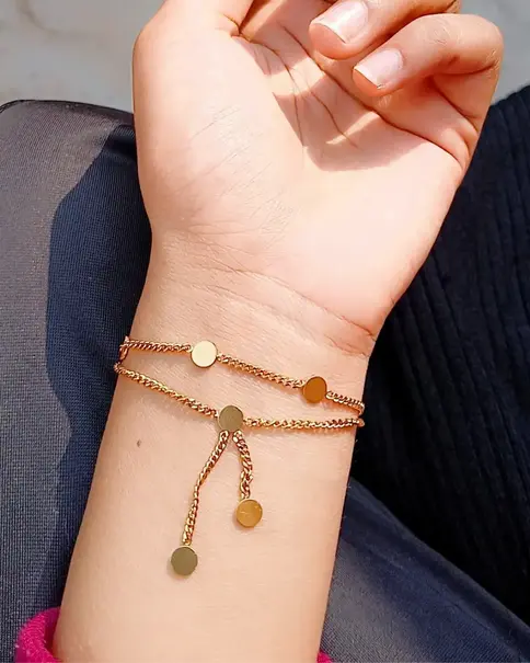 Wrist wearing a gold-toned two-layered bracelet with disc charms.