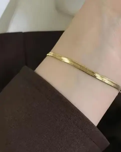 Wrist wearing a gold-toned flat snake chain bracelet.