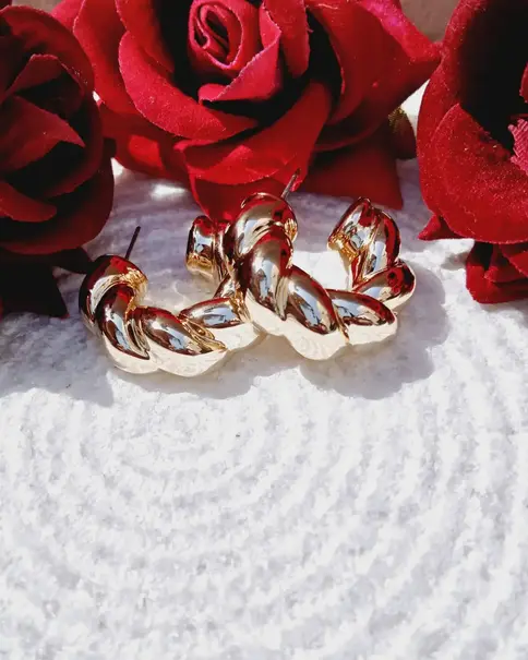 Rose gold twisted hoops on white with red roses.