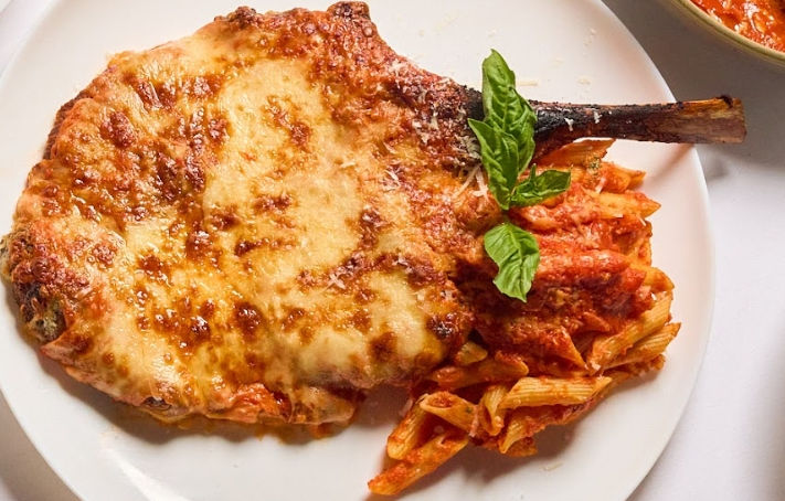 veal chop with penne pasta and basil on white plate