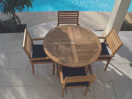 Four teak dining chairs surrounding a round teak dining table outside.