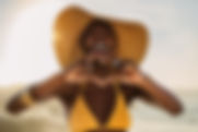 Smiling woman in bikini standing on the beach making a heart shape with her fingers. Femal