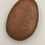 Thumbnail: Back side of hand-painted mandala stone showing natural stone surface with artist signature.