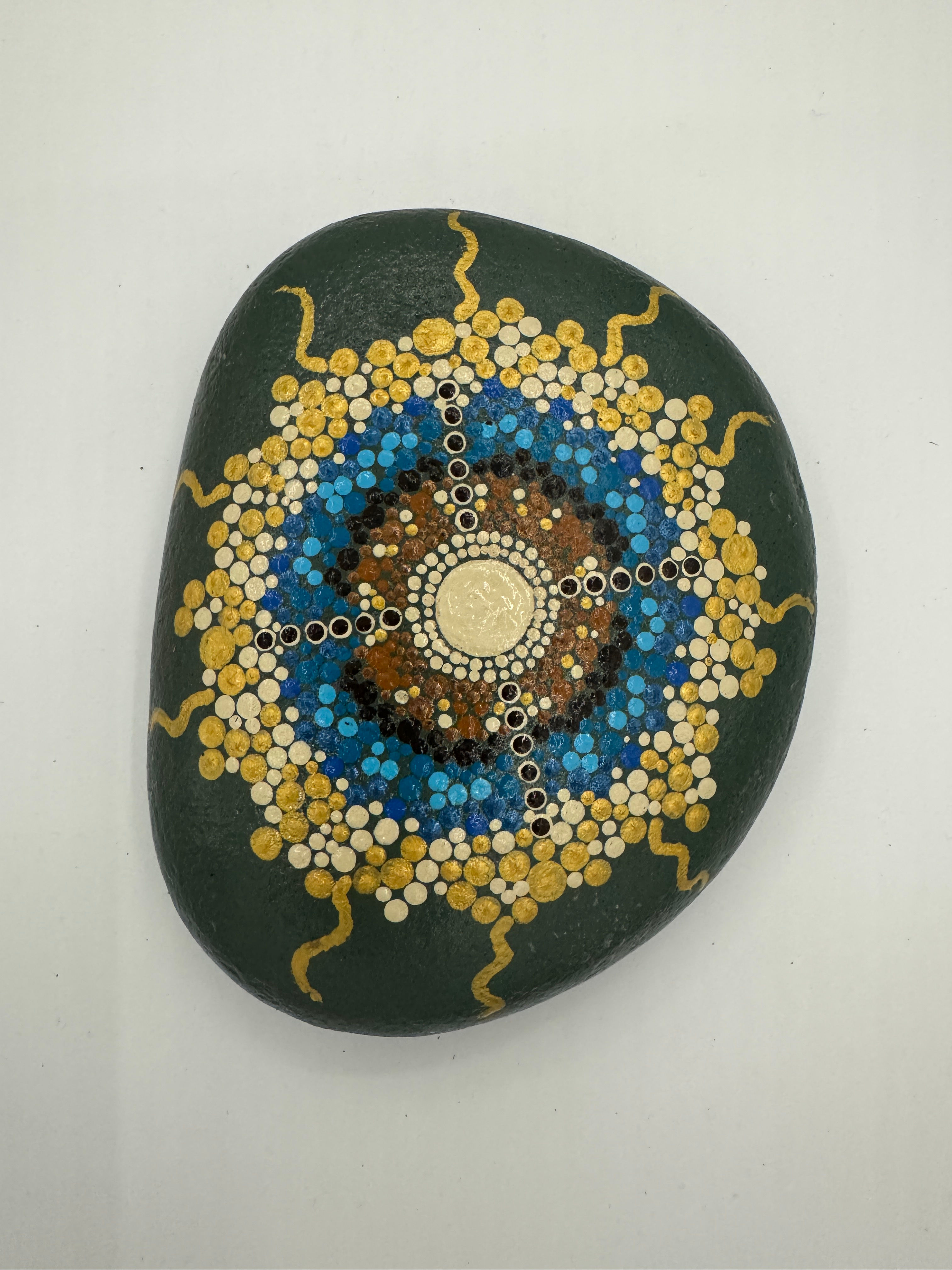 Hand-painted mandala stone with deep blue, turquoise, gold, and white intricate patterns, radiating from a central floral des