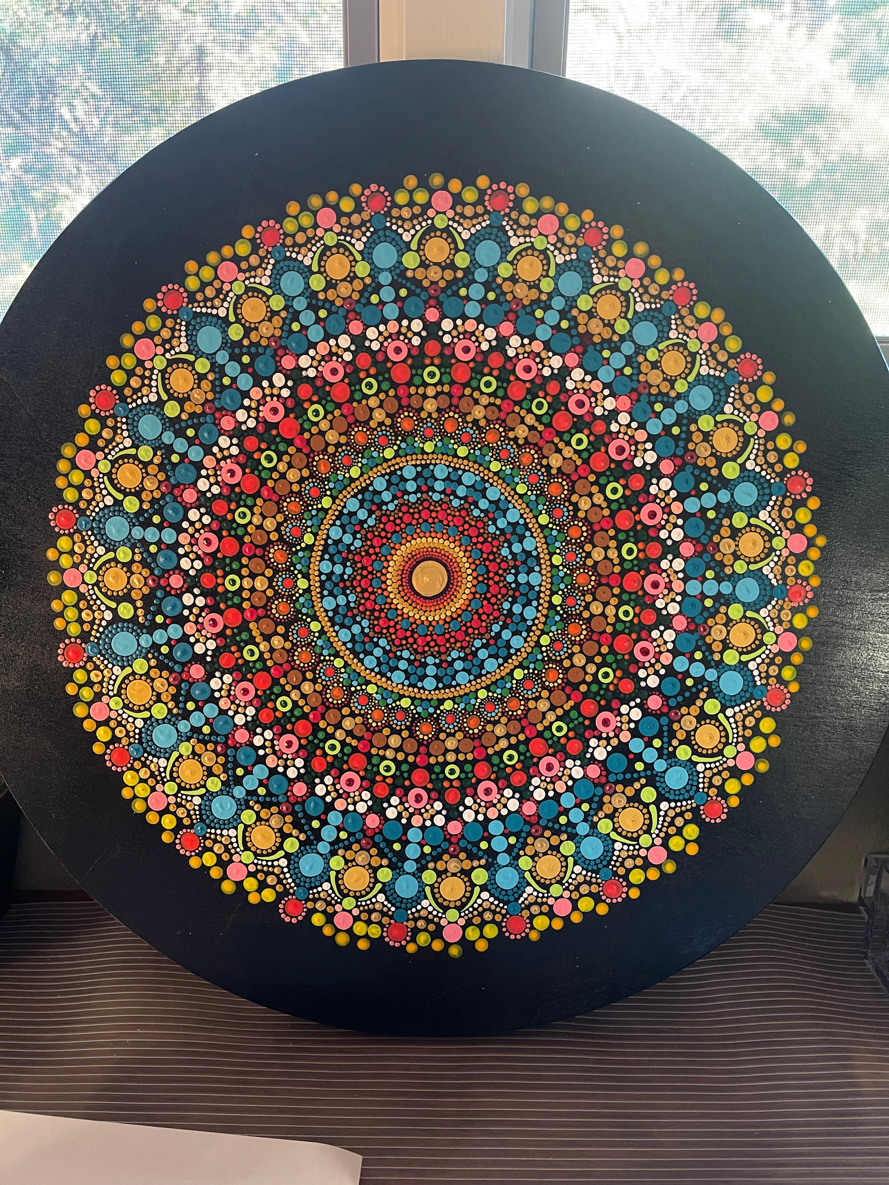 Hand-painted mandala on a birch wood wheel featuring vibrant orange, turquoise, green, and yellow circular patterns.