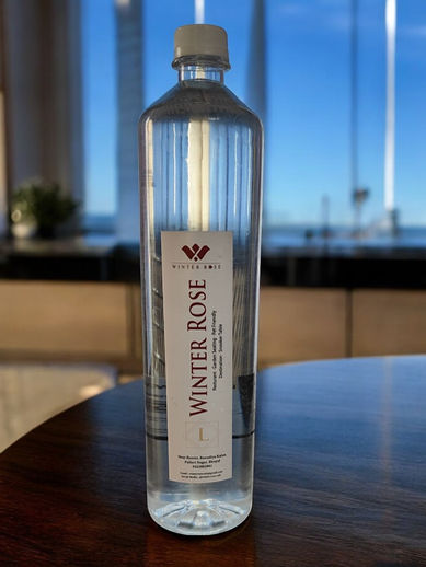 Clear water bottle with "Winter Rose" label on wooden table, sky background.