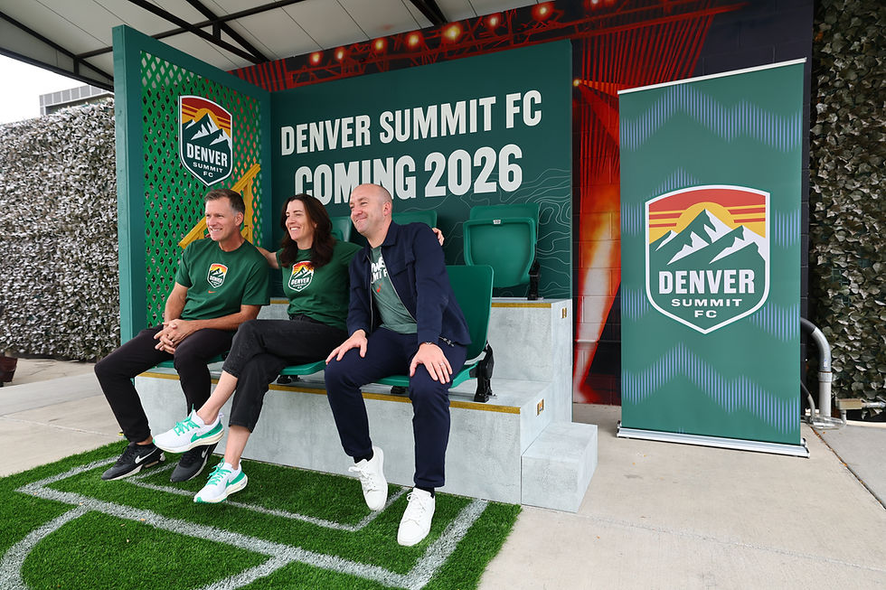 Three smiling adults sit on a soccer bench at a Denver Summit FC Kick-off rally event.