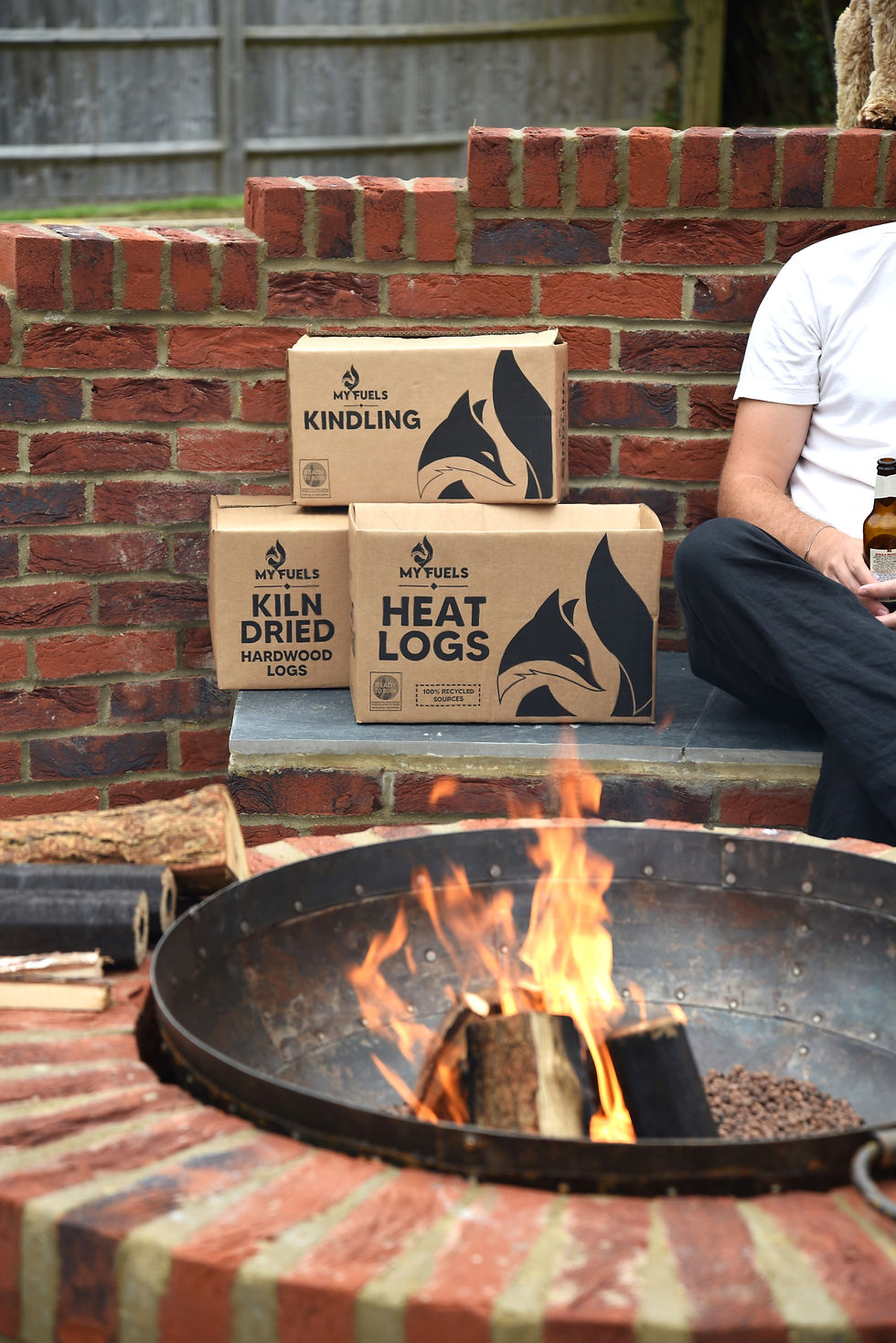 Thumbnail: man next to a lit fire pit with boxes of kiln dired hardwood logs