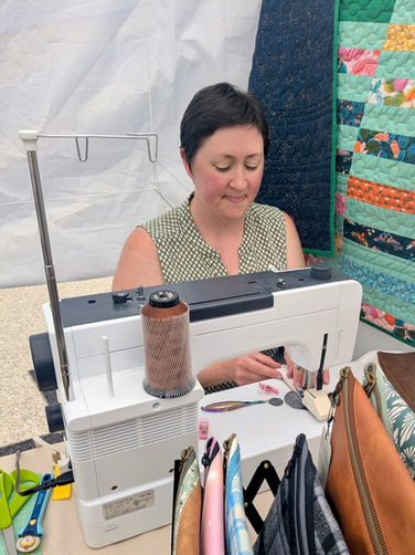 A woman sitting in an outdoor tent at a sewing machine, sewing a pouch.
