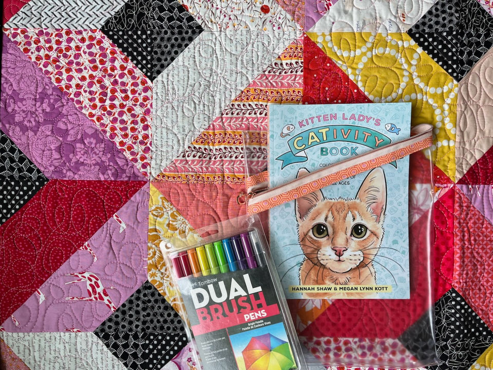Quilt with vinyl activity book pouch, activity book and markers laying on top.