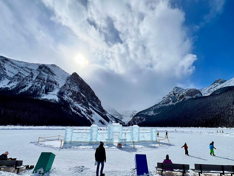 Snowy mountain valley with an ice castle on a frozen lake, people walking and skiing under a bright cloudy blue sky