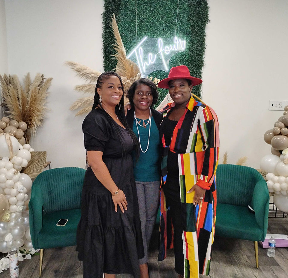 Clara Throckmorton posing with two women in front of a greenery wall and balloon decor at an indoor event