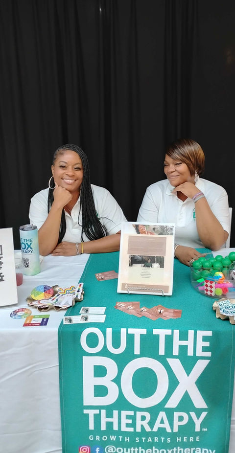 Clara Throckmorton and a colleague sitting behind an Out the Box Therapy vendor table at a community event