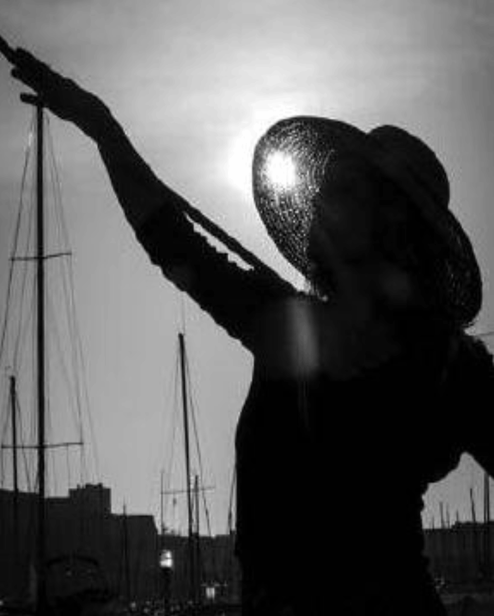Joëlle Viaud – silhouette of woman in hat with raised arm, black and white marina background with sailboats.