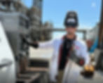 Welder in a white FR jacket operating welding equipment and smiling at the camera.