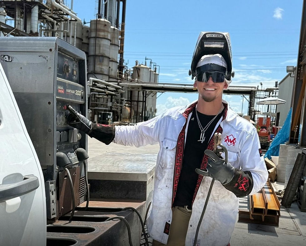 Welder in a white FR jacket operating welding equipment and smiling at the camera.