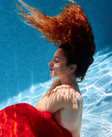 Photo sous l'eau de selflove dans une piscine d'une femme s'enlaçant dans un tissu rouge