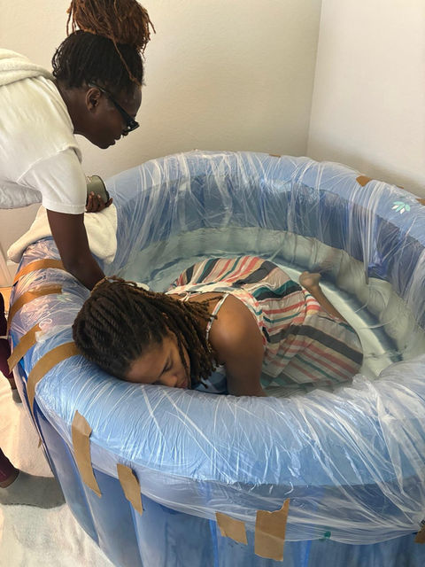 Woman giving birth in water birth tub assisted by midwife