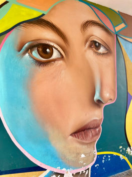 A large-scale sidewalk mural in Málaga showing a detailed face outlined in neon pink. The figure gazes upward with expressive eyes, surrounded by colorful geometric patterns on a textured city wall.