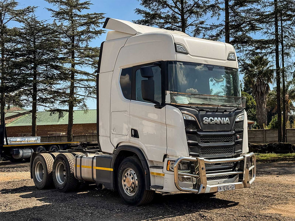 White Scania truck parked on gravel in front of trees.