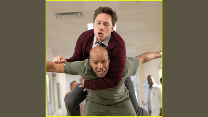 Zach Braff in a maroon cardigan jumping onto Donald Faison’s back for an "Eagle" pose in the Scrubs Reboot Teaser, recreating their iconic bromance.