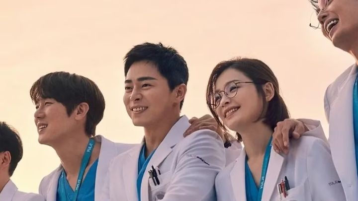 Close-up of three Hospital Playlist cast members, two men and one woman, smiling and wearing white doctor coats.