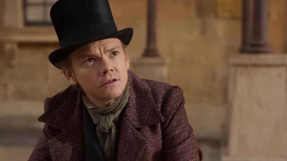 Thomas Brodie-Sangster wears a top hat and patterned coat, gazing upward with a guarded expression in a scene from The Artful Dodger.