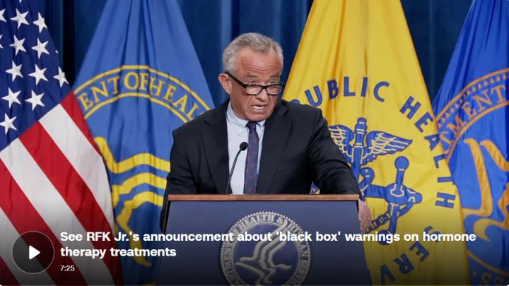 RFK Jr. speaks at a podium with American and Department of Health flags in the background, discussing black box warnings on hormone therapy.