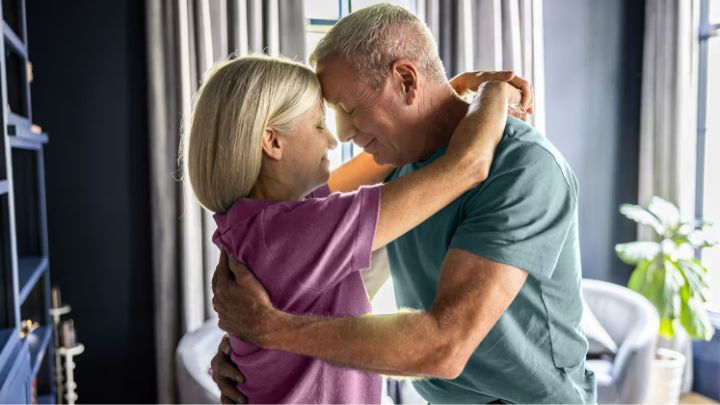 Happy grey-haired senior couple dancing at home, embracing with joy to illustrate a healthy retirement lifestyle and wellness in their living room.