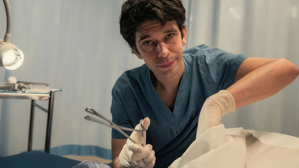 Ben Whishaw as Adam Kay in This Is Going to Hurt, breaking the fourth wall while holding surgical forceps and wearing blue medical scrubs.