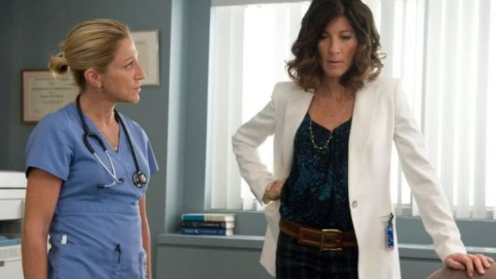 Edie Falco as Nurse Jackie Peyton in scrubs, conversing with a woman in a white blazer. Her Nurse Jackie revival status remains uncertain.