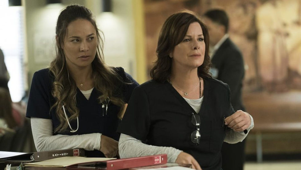 Marcia Gay Harden and Moon Bloodgood in the Code Black TV series, standing behind a hospital nursing station desk with patient charts and files.