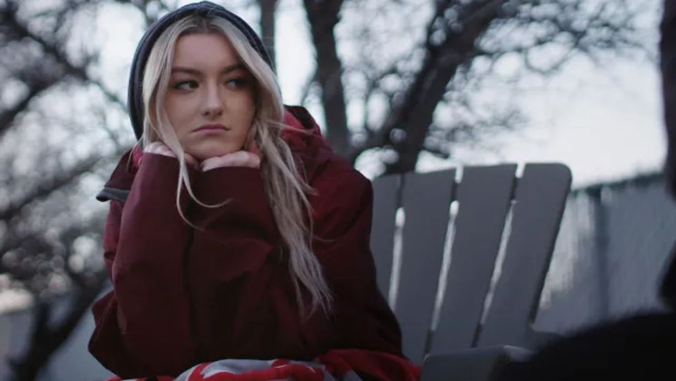 Una joven pensativa con una chaqueta roja se sienta al aire libre, reflejando los desafíos emocionales y médicos que enfrentan los pacientes en la docuserie Diagnosis de Netflix.