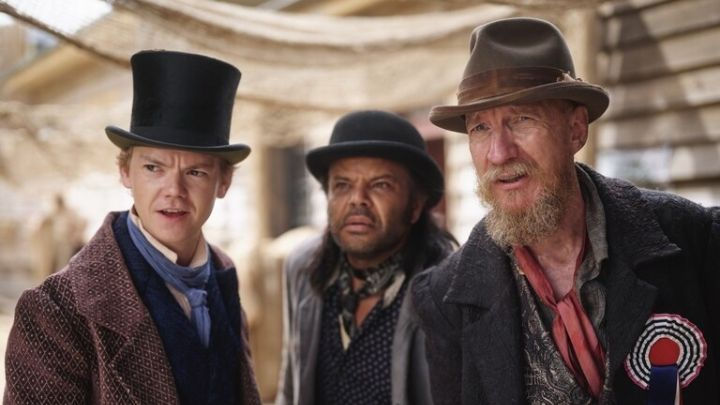 Jack Dawkins, Tim Billiberllary, and Fagin stand together in a colonial Australian market, ready for fresh schemes in The Artful Dodger Season 2.
