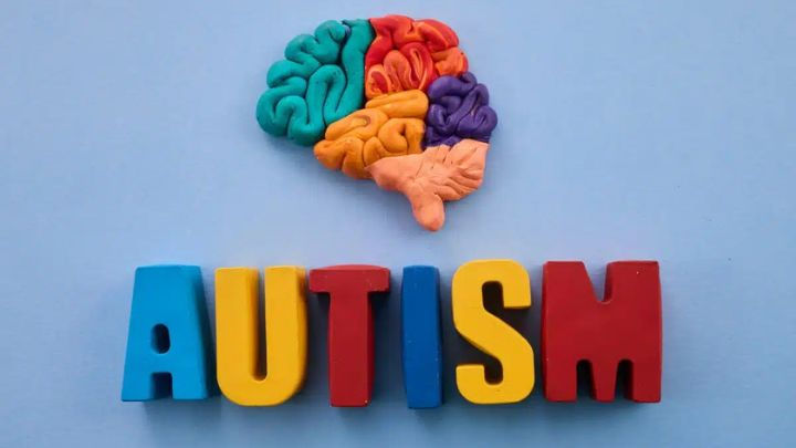Multicolored clay brain model representing neurodevelopment positioned above colorful block letters spelling the word autism on a blue background.