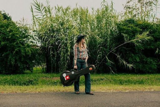 Toria Richings stands on a road with her guitar case facing away from the camera