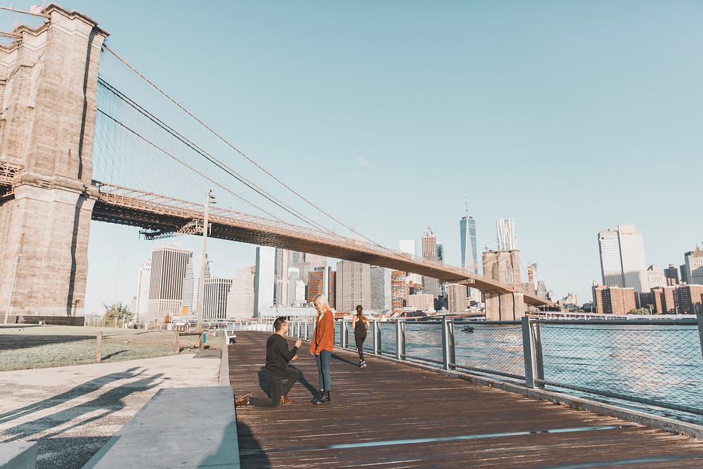 A man proposing to his girlfriend under the Brooklyn Bridge in New York.