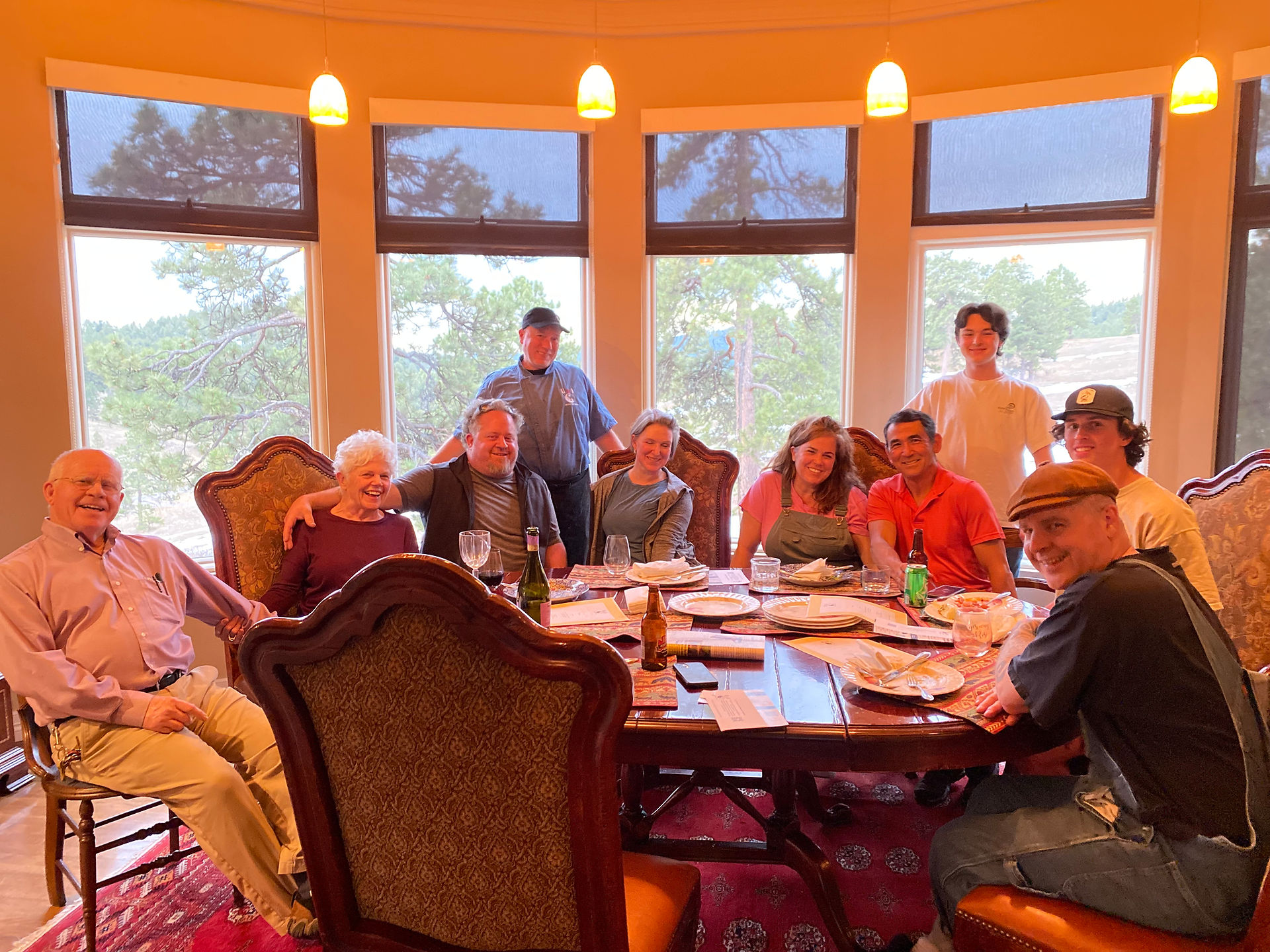 A large round table with a family of 9 men and woman of different ages posing around a dinner table.